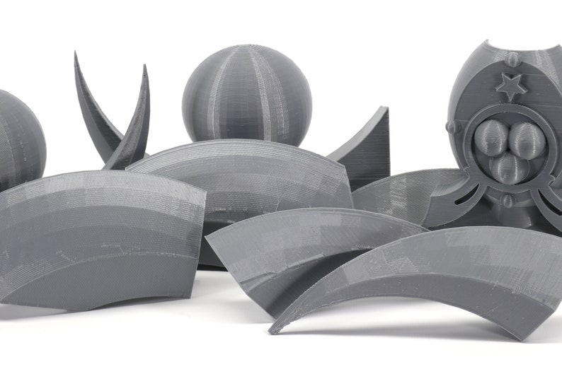 May include: A collection of gray 3D printed objects, including spheres, arches, and a more complex object with a star and three spheres. The objects are arranged on a white surface.