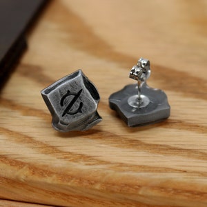 May include: A pair of silver earrings with a textured, geometric design. Each earring features a small, black symbol.