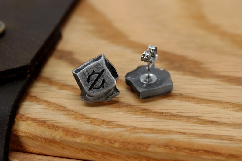 May include: A pair of silver earrings with a textured, geometric design. Each earring features a small, black symbol.