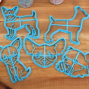 Puede incluir: Cinco cortadores de galletas de pl&aacute;stico azul con forma de diferentes variaciones de un perro chihuahua. Los cortadores est&aacute;n sobre una superficie de madera.