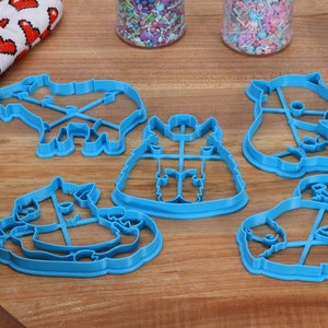May include: Five blue plastic cookie cutters shaped like animals. The cutters are on a wooden surface. The cutters are for making cookies in the shapes of a unicorn, a cat, a panda, a llama, and a reindeer.