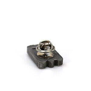 May include: A gray metal pin in the shape of a cassette tape with a silver metal pin back.