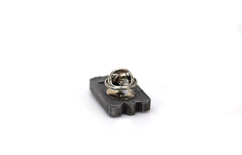 May include: A gray metal pin in the shape of a cassette tape with a silver metal pin back.