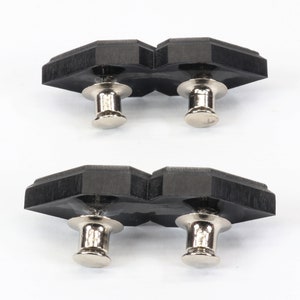 May include: Two black, geometric-shaped push pins with silver-colored metal posts and heads. The push pins are arranged in two sets of two, with a white background.
