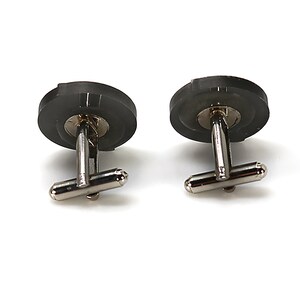 May include: A pair of silver cufflinks with black round tops. The cufflinks have a simple design.