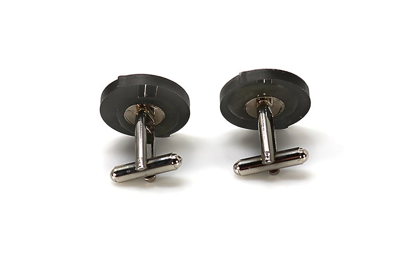 May include: A pair of silver cufflinks with black round tops. The cufflinks have a simple design.