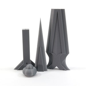 May include: Three gray 3D printed objects, two are tall and narrow, one is short and wide, with a round gray object in the front.