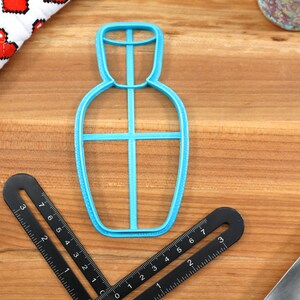 May include: A blue plastic cookie cutter shaped like a bottle with a cross-shaped design inside.