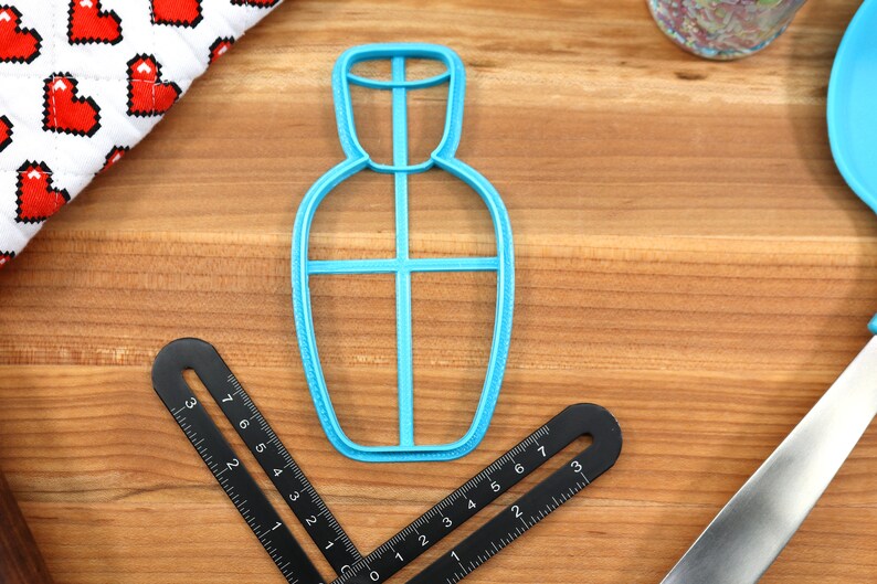May include: A blue plastic cookie cutter shaped like a bottle with a cross-shaped design inside.