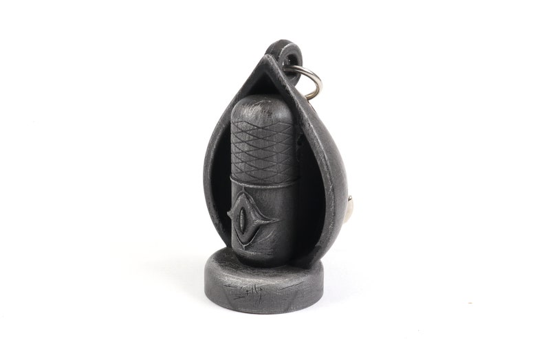 May include: A black metal keychain shaped like a teardrop with a smaller black metal cylinder inside. The cylinder has a diamond-shaped design and a silver ring attached to the top.