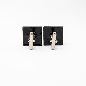 May include: A pair of black square cufflinks with silver-toned accents.
