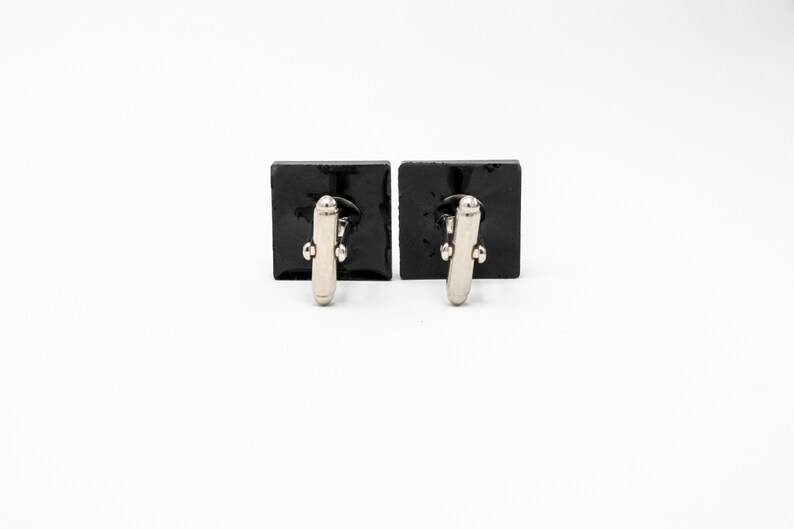 May include: A pair of black square cufflinks with silver-toned accents.