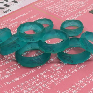 May include: A close-up of nine teal-colored plastic rings with numbers printed on them. The rings are stacked on top of each other and are on a pink surface.