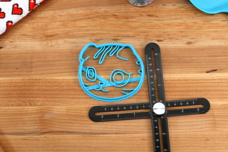 May include: A blue plastic cookie cutter shaped like a cat's face. The cutter is about 2 inches wide and 2 inches tall.