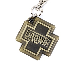 May include: A gold-colored metal keychain shaped like a cross with the word "GROWTH" written on it.