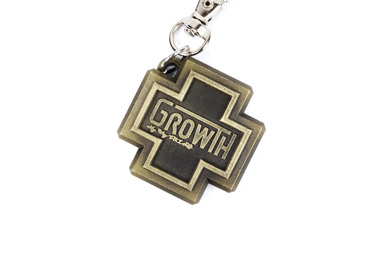 May include: A gold-colored metal keychain shaped like a cross with the word "GROWTH" written on it.