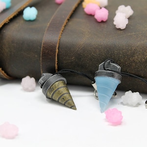 May include: Two keychains with drill bit designs. One keychain is blue and the other is gold and brown. Both keychains are hanging from a brown leather journal.