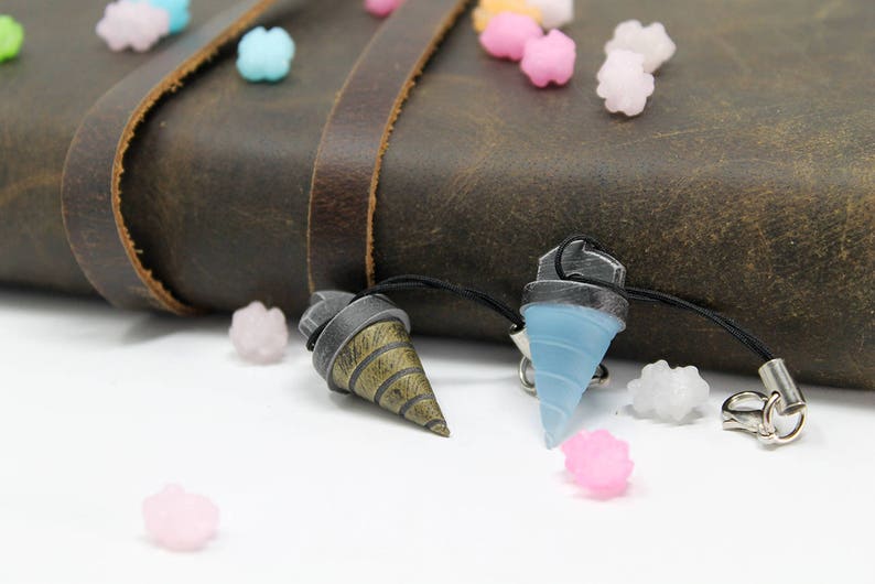 May include: Two keychains with drill bit designs. One keychain is blue and the other is gold and brown. Both keychains are hanging from a brown leather journal.