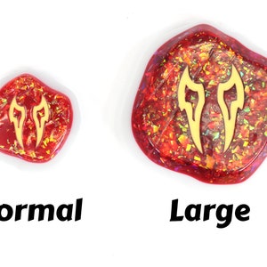 May include: Two resin cabochons with a gold glitter finish and a gold flame design. The cabochon on the left is labeled "Normal" and the cabochon on the right is labeled "Large".