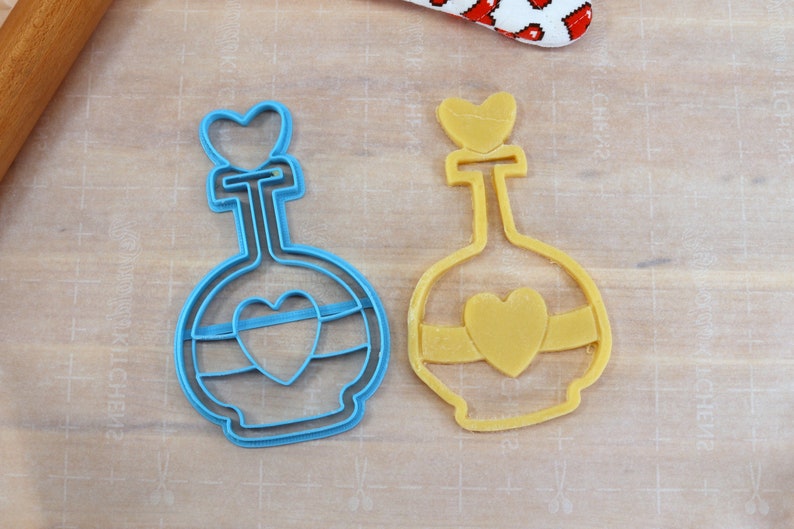 May include: Two cookie cutters in the shape of a bottle with a heart on top. The bottle on the left is blue and the bottle on the right is yellow.