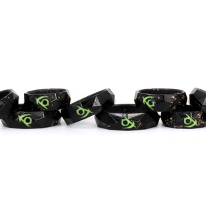 May include: A set of six black silicone rings with a green and gold design. The rings are stacked on top of each other.