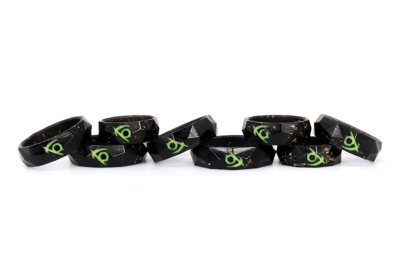 May include: A set of six black silicone rings with a green and gold design. The rings are stacked on top of each other.
