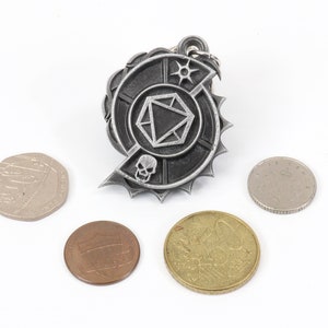 May include: A silver metal keychain with a circular design featuring a skull, a die, and a star. The keychain is surrounded by a jagged edge and is surrounded by four coins.