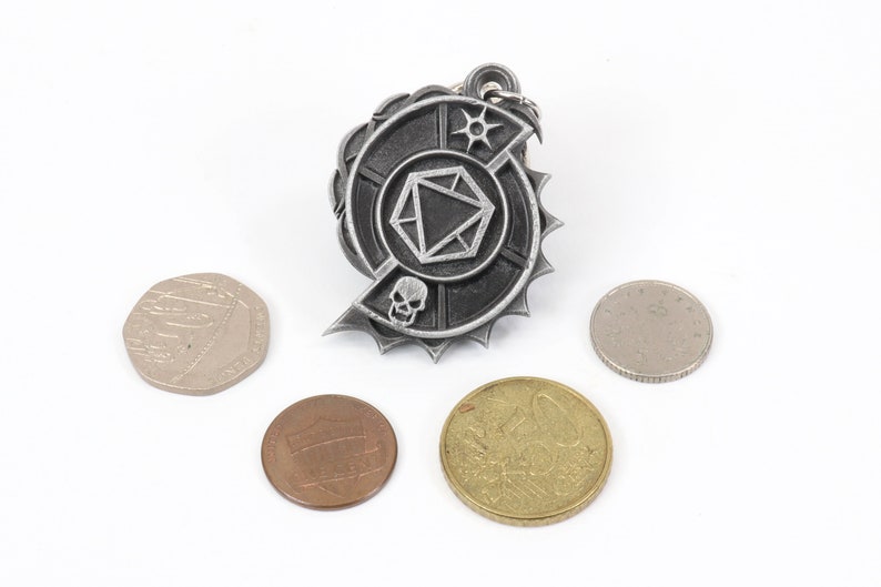 May include: A silver metal keychain with a circular design featuring a skull, a die, and a star. The keychain is surrounded by a jagged edge and is surrounded by four coins.