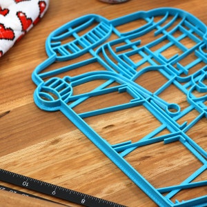 May include: A blue plastic cookie cutter shaped like a pair of coffee cups. The cookie cutter is on a wooden surface.