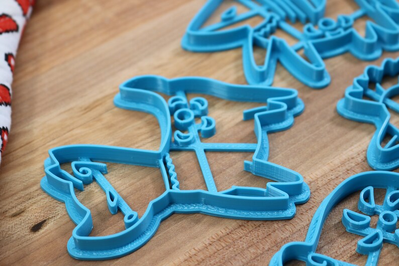 Puede incluir: Un juego de cortadores de galletas de pl&aacute;stico azul con forma de varios dise&ntilde;os navide&ntilde;os. Los cortadores est&aacute;n sobre una superficie de madera.