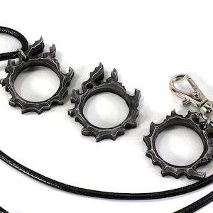 Puede incluir: Tres anillos de metal de color plateado con un dise&ntilde;o de llama, uno unido a un cord&oacute;n negro con un cierre plateado.