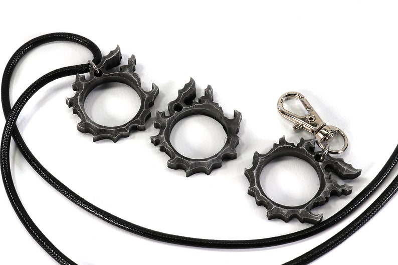 Puede incluir: Tres anillos de metal de color plateado con un dise&ntilde;o de llama, uno unido a un cord&oacute;n negro con un cierre plateado.