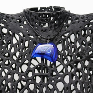 May include: A blue glass pendant necklace with a symbol on it. The necklace is on a black mannequin.