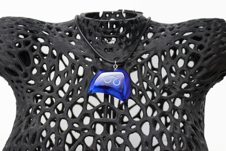 May include: A blue glass pendant necklace with a symbol on it. The necklace is on a black mannequin.