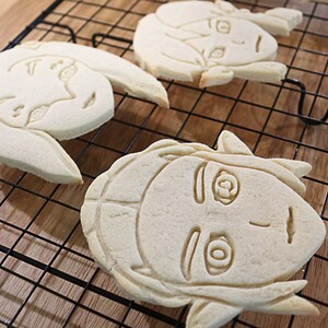 May include: Three sugar cookies decorated with icing in the shape of cartoon faces. The cookies are on a black wire cooling rack.