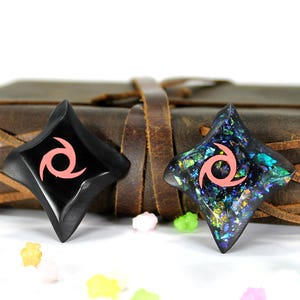 Pu&ograve; includere: Due stelle ninja nere a forma di stella con un design a spirale rosa. Una stella &egrave; realizzata in un materiale nero liscio, mentre l'altra &egrave; realizzata in un materiale nero scintillante con riflessi blu e verdi iridescenti.