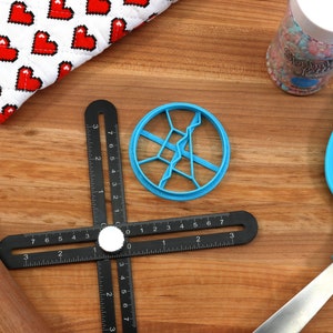 May include: A blue plastic cookie cutter shaped like a starburst with a black ruler and a wooden rolling pin on a wooden surface.
