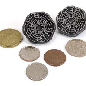 May include: Two silver-colored, octagonal-shaped, geometric designs with a raised, intricate pattern. The designs are similar to a honeycomb or a web. The designs are surrounded by five coins.