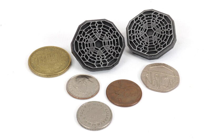 May include: Two silver-colored, octagonal-shaped, geometric designs with a raised, intricate pattern. The designs are similar to a honeycomb or a web. The designs are surrounded by five coins.