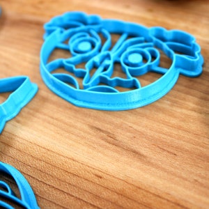 May include: A set of blue plastic cookie cutters shaped like cartoon animals. The cutters are on a wooden surface.