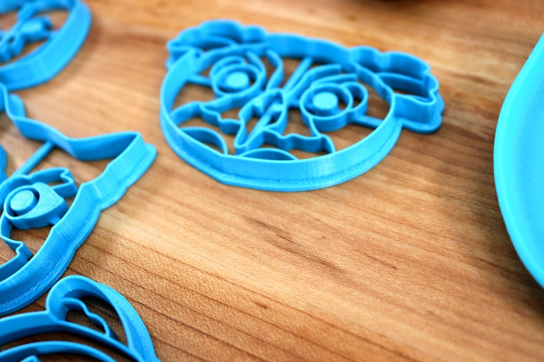 May include: A set of blue plastic cookie cutters shaped like cartoon animals. The cutters are on a wooden surface.