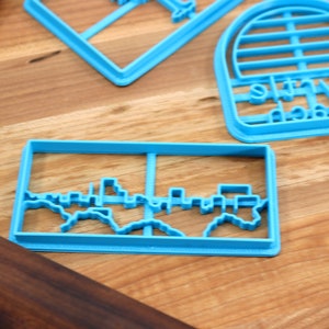 May include: A set of blue plastic cookie cutters, including a skyline, a beach umbrella, and a "My Beach" sign.