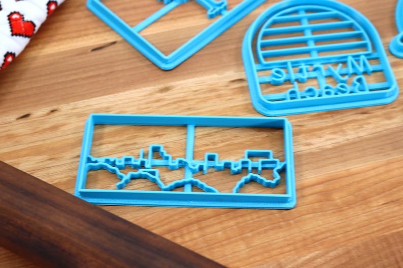 May include: A set of blue plastic cookie cutters, including a skyline, a beach umbrella, and a "My Beach" sign.