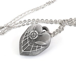 May include: A silver heart-shaped pendant necklace with a detailed design of a cross and a web-like pattern. The chain is silver and has a delicate link style.