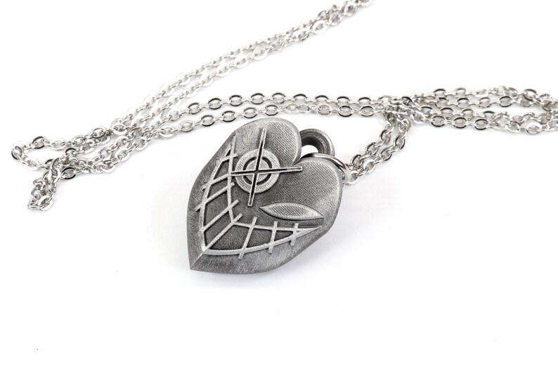May include: A silver heart-shaped pendant necklace with a detailed design of a cross and a web-like pattern. The chain is silver and has a delicate link style.