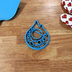 May include: A blue plastic cookie cutter shaped like a flame with a circle and smaller circles around it.
