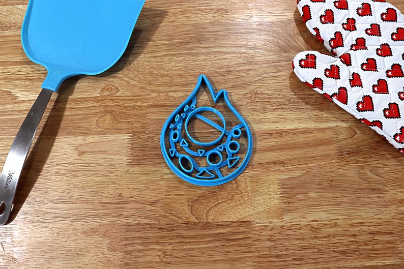 May include: A blue plastic cookie cutter shaped like a flame with a circle and smaller circles around it.