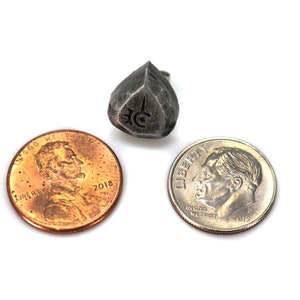 May include: A silver metal die with a symbol on each side. The die is about the size of a US penny.