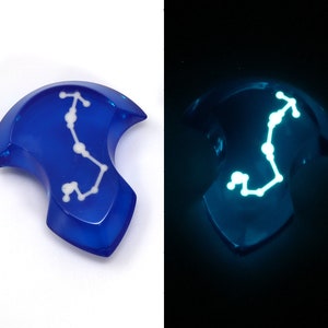 May include: A blue resin pendant with a white constellation design that glows in the dark.