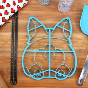May include: Blue plastic cookie cutter shaped like a dog's rear end. The cutter has a grid pattern and is designed to make multiple cookies at once.